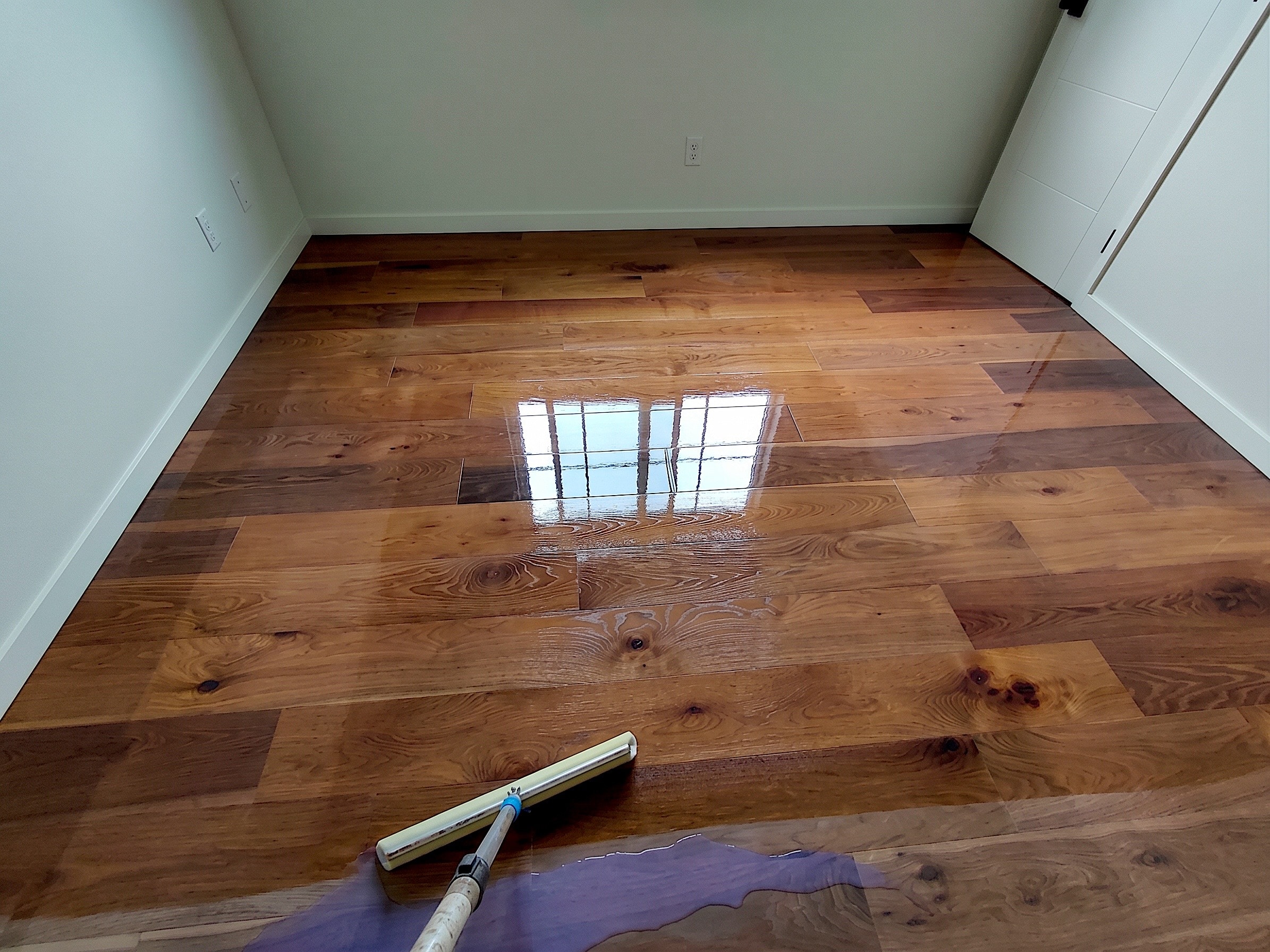 Top coat being applied to wide plank hardwood floor